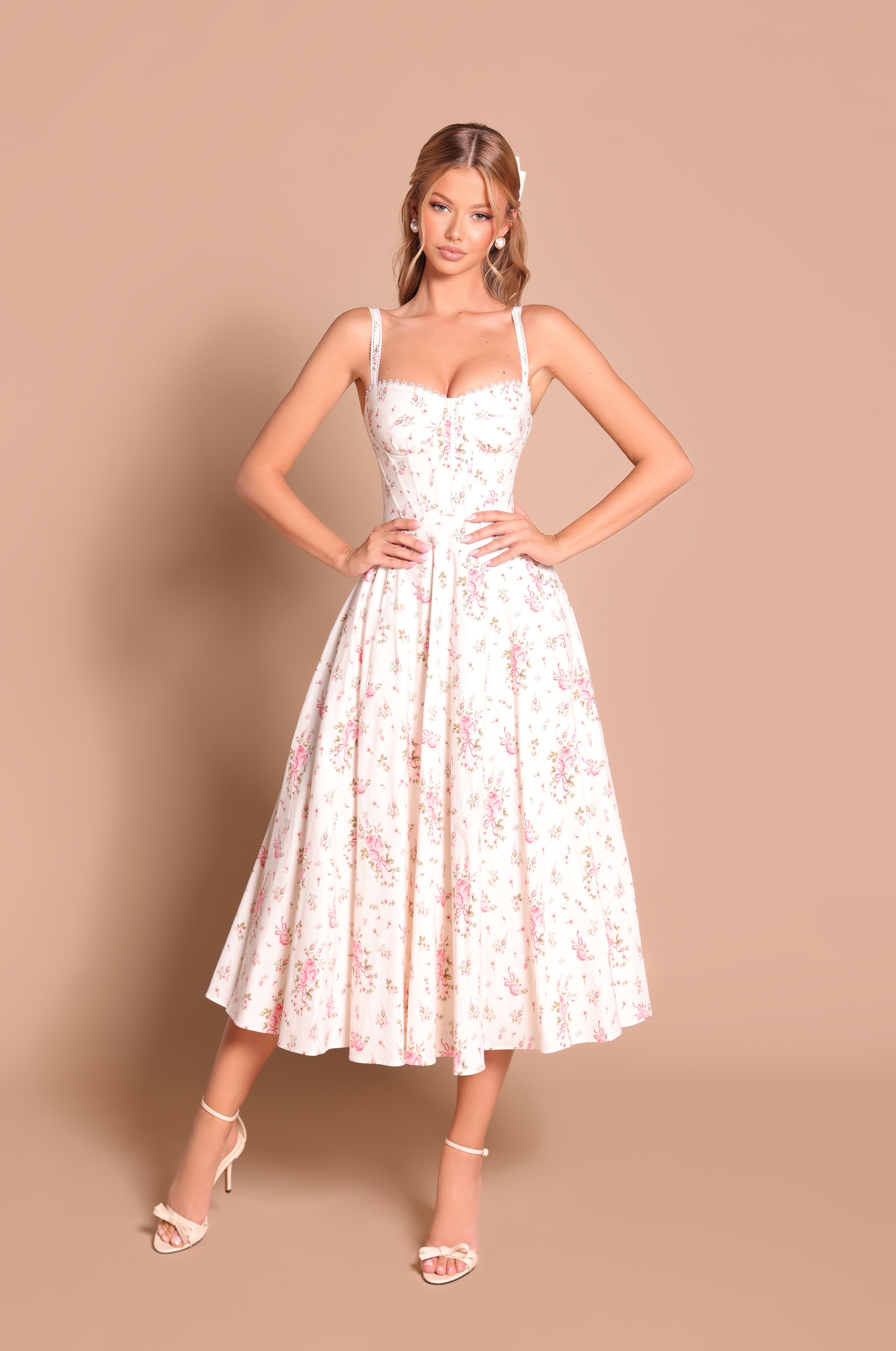A woman stands against a beige background wearing the Rosella, a cream white floral casual midi dress with a fitted corset bodice and full skirt.